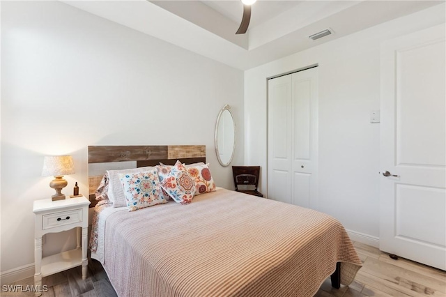 bedroom with ceiling fan, wood finished floors, visible vents, baseboards, and a closet