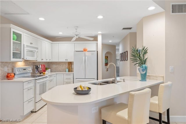 kitchen featuring white cabinetry, sink, kitchen peninsula, white appliances, and a kitchen bar