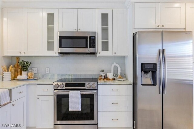 kitchen with tasteful backsplash, appliances with stainless steel finishes, glass insert cabinets, and white cabinets