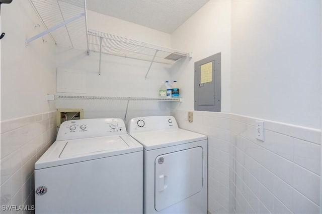 washroom with a wainscoted wall, tile walls, washing machine and dryer, laundry area, and electric panel