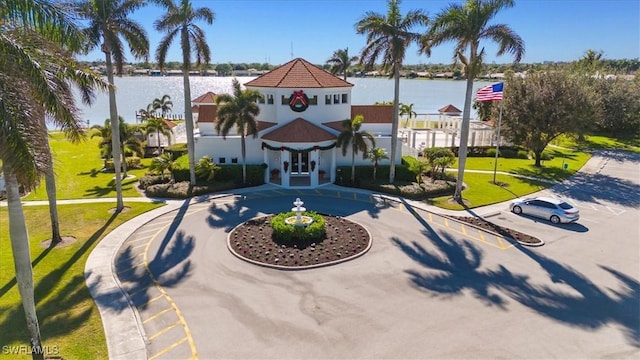 exterior space with uncovered parking, a water view, curved driveway, and a lawn