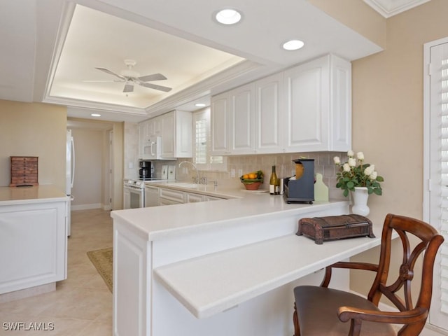 kitchen featuring a raised ceiling, white cabinetry, white appliances, and kitchen peninsula