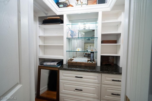 interior space featuring ornamental molding, dark stone countertops, white cabinets, and built in shelves