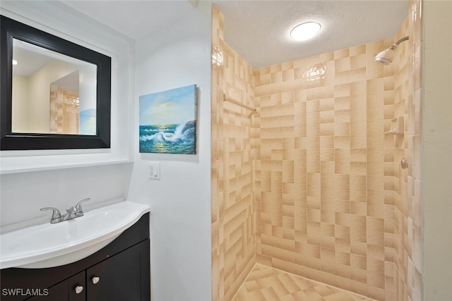 bathroom with a textured ceiling, vanity, and tiled shower