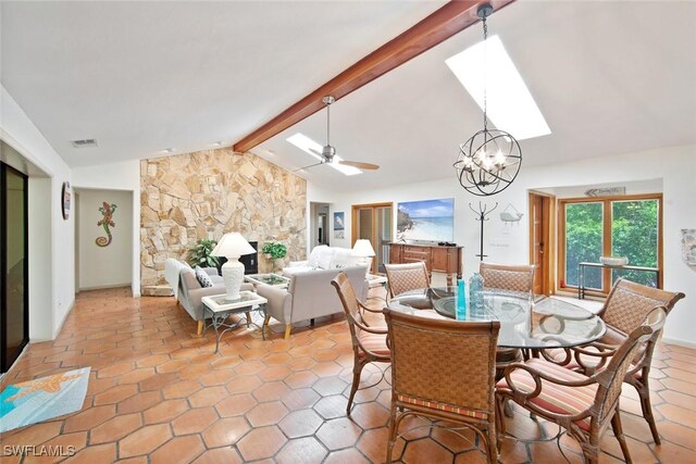 dining space featuring lofted ceiling with skylight, a fireplace, ceiling fan with notable chandelier, and tile patterned flooring