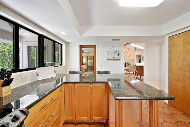 kitchen featuring a kitchen bar, kitchen peninsula, and dark stone counters