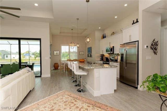 kitchen featuring appliances with stainless steel finishes, pendant lighting, a center island with sink, light hardwood / wood-style flooring, and white cabinetry