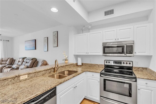 kitchen featuring kitchen peninsula, stainless steel appliances, light stone countertops, white cabinets, and sink