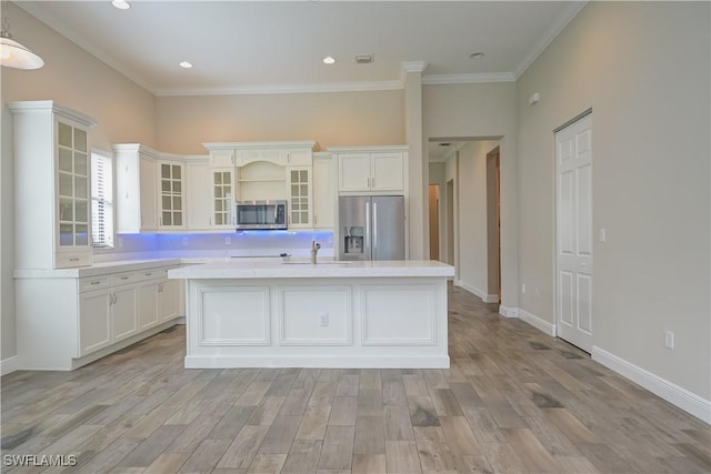 kitchen with appliances with stainless steel finishes, light wood-type flooring, crown molding, a center island with sink, and white cabinets