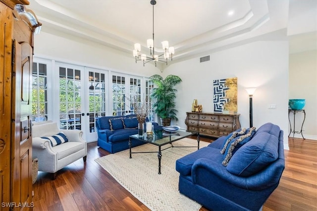 living room featuring french doors, dark hardwood / wood-style floors, a raised ceiling, and a chandelier