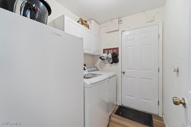 laundry area with cabinets, washing machine and dryer, and light hardwood / wood-style flooring