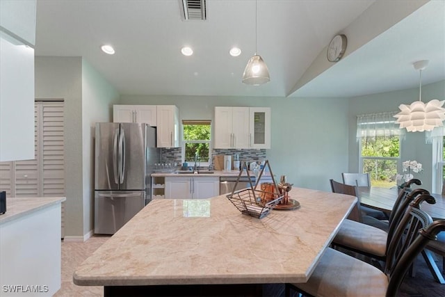 kitchen featuring sink, hanging light fixtures, decorative backsplash, appliances with stainless steel finishes, and white cabinetry