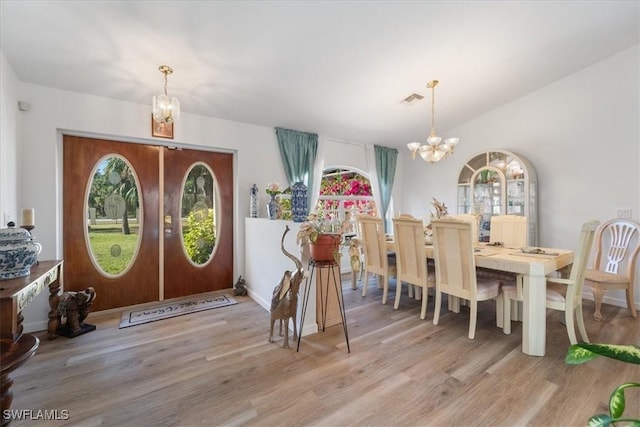 dining room with a notable chandelier, light wood-type flooring, a wealth of natural light, and french doors