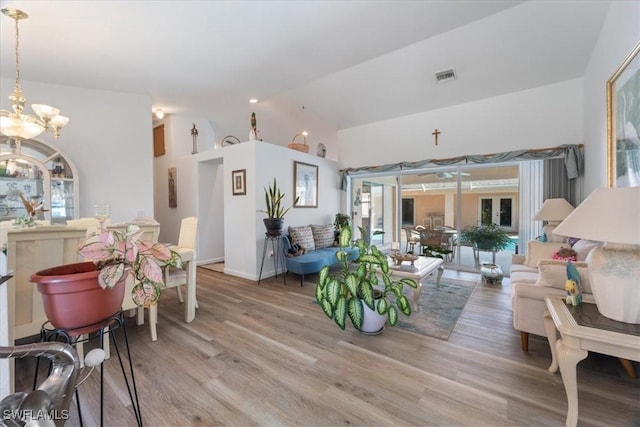 living room with a chandelier, light wood-type flooring, and vaulted ceiling