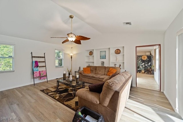 living room featuring lofted ceiling, light wood-type flooring, built in features, and a healthy amount of sunlight