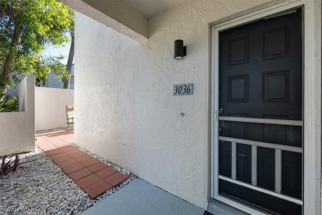 view of exterior entry with fence and stucco siding