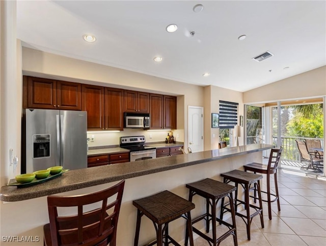 kitchen featuring a kitchen breakfast bar, light tile patterned floors, lofted ceiling, and appliances with stainless steel finishes