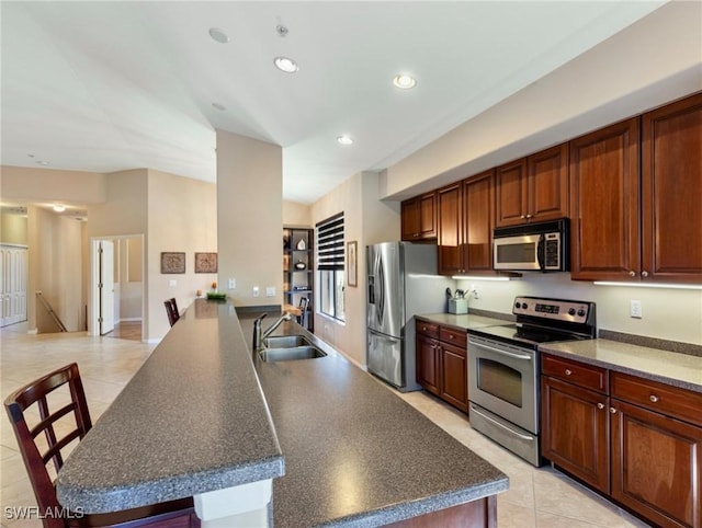 kitchen with kitchen peninsula, appliances with stainless steel finishes, sink, light tile patterned floors, and a breakfast bar area