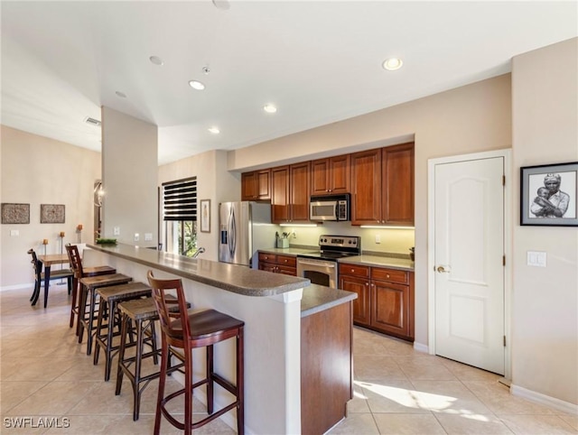 kitchen with a breakfast bar area, kitchen peninsula, light tile patterned floors, and appliances with stainless steel finishes