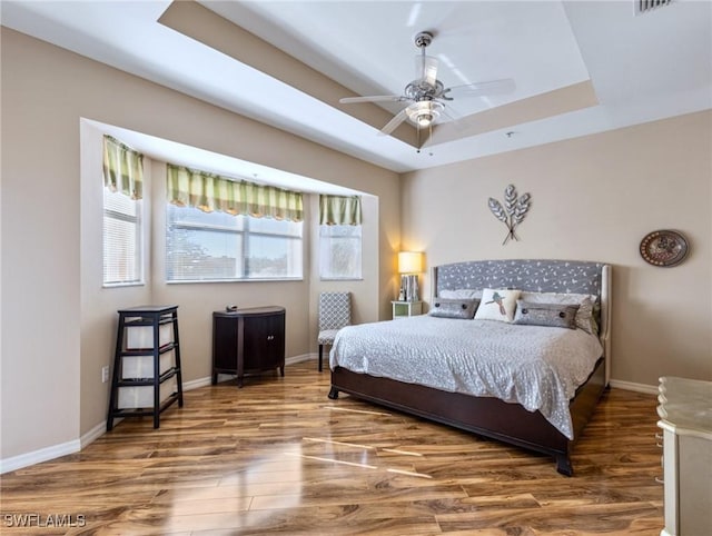 bedroom featuring a raised ceiling, ceiling fan, and wood-type flooring