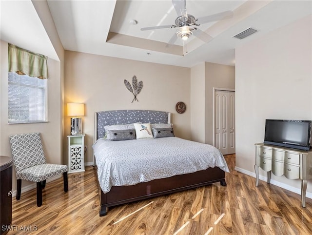 bedroom with a closet, hardwood / wood-style flooring, ceiling fan, and a tray ceiling