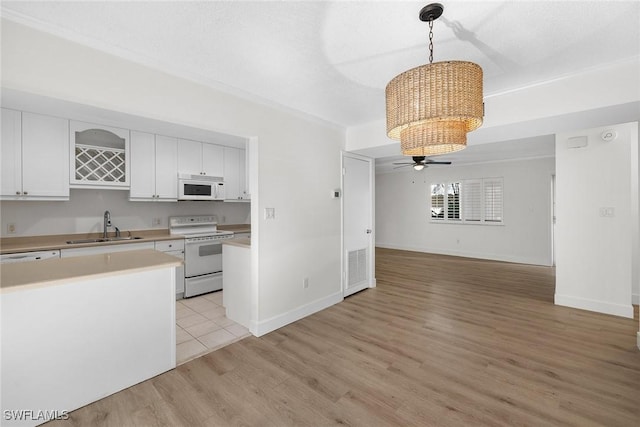 kitchen featuring light wood-type flooring, white appliances, sink, pendant lighting, and white cabinets