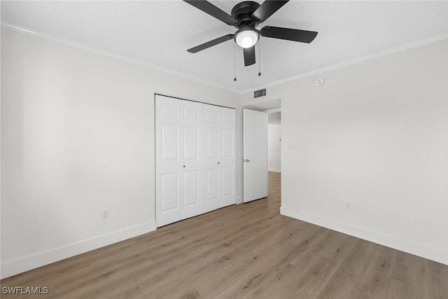 unfurnished bedroom with ceiling fan, light wood-type flooring, crown molding, and a closet