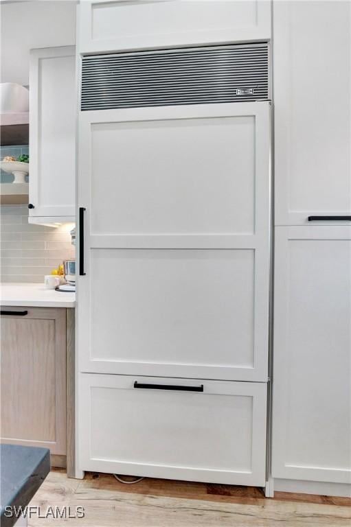 room details with white cabinets, paneled built in refrigerator, backsplash, and light hardwood / wood-style flooring