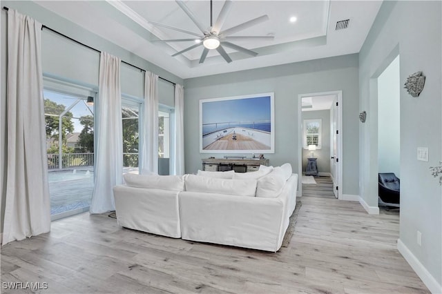 living room with a tray ceiling, ceiling fan, and light wood-type flooring