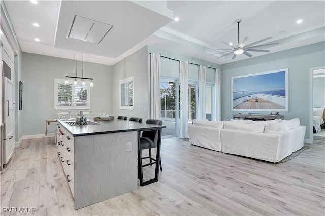 kitchen with light wood-type flooring, a raised ceiling, decorative light fixtures, white cabinets, and a center island