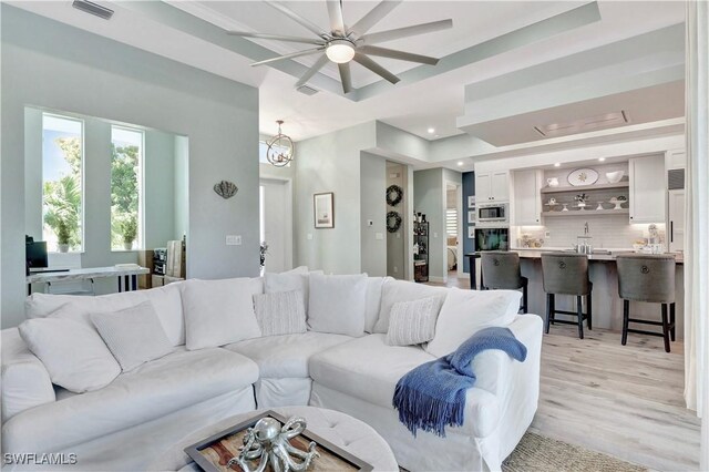 living room with a raised ceiling, light hardwood / wood-style flooring, and ceiling fan with notable chandelier