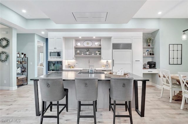 kitchen with white cabinets, a large island with sink, built in appliances, and a breakfast bar area