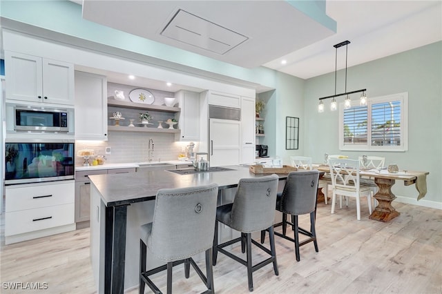 kitchen featuring a kitchen island with sink, white cabinets, sink, built in appliances, and tasteful backsplash