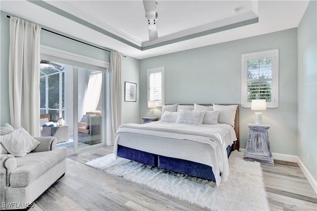 bedroom featuring a tray ceiling, access to exterior, light hardwood / wood-style flooring, and multiple windows