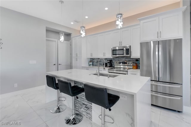 kitchen featuring pendant lighting, a center island with sink, white cabinets, sink, and appliances with stainless steel finishes