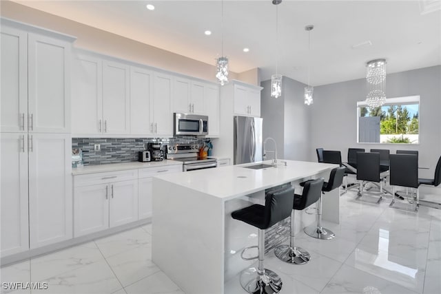 kitchen featuring stainless steel appliances, pendant lighting, decorative backsplash, a center island with sink, and white cabinets