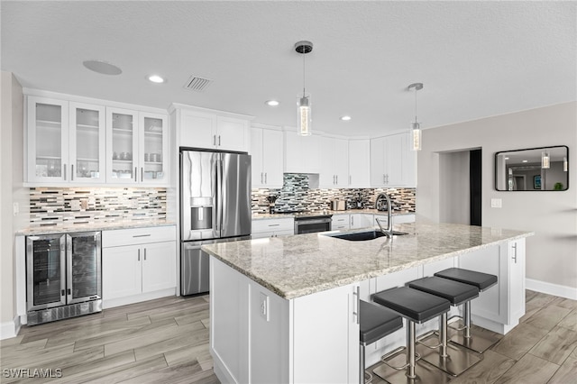 kitchen with sink, beverage cooler, stainless steel appliances, an island with sink, and white cabinets