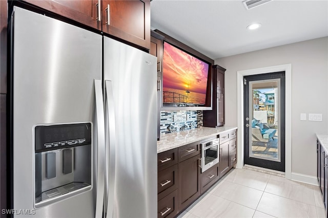 kitchen with light stone countertops, stainless steel refrigerator with ice dispenser, dark brown cabinetry, and light tile patterned floors