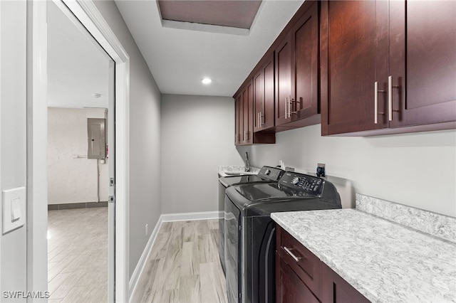 clothes washing area with cabinets, light wood-type flooring, electric panel, and washing machine and dryer