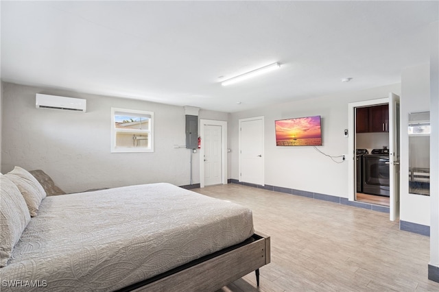 bedroom featuring washer and clothes dryer, baseboards, light wood-style floors, and a wall unit AC