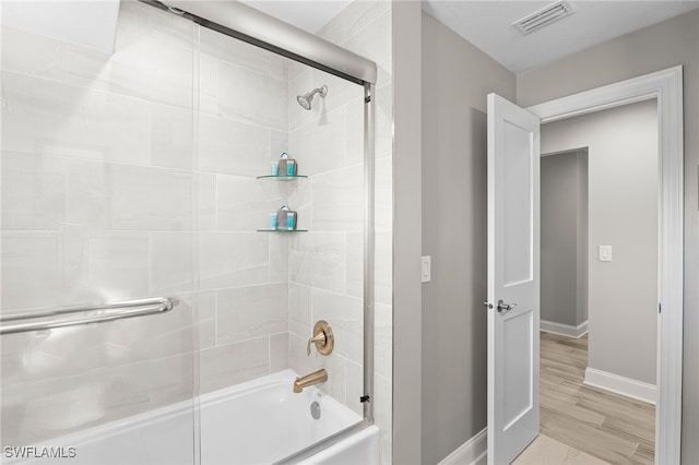 bathroom featuring combined bath / shower with glass door, visible vents, baseboards, and wood finished floors