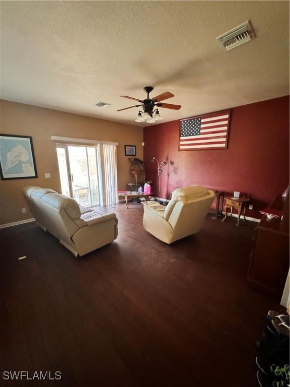 living room with a textured ceiling, ceiling fan, and dark hardwood / wood-style floors