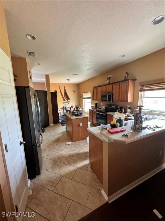 kitchen with a textured ceiling, stainless steel appliances, a kitchen island, and a wealth of natural light