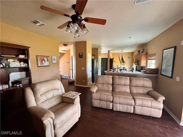 living room with a textured ceiling, ceiling fan, and dark wood-type flooring