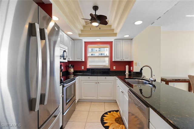 kitchen featuring dark stone counters, stainless steel appliances, a raised ceiling, sink, and white cabinetry