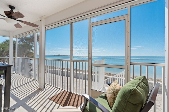 sunroom / solarium with ceiling fan, a water view, and a view of the beach