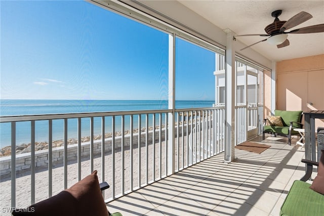 sunroom / solarium featuring ceiling fan, a water view, and a beach view