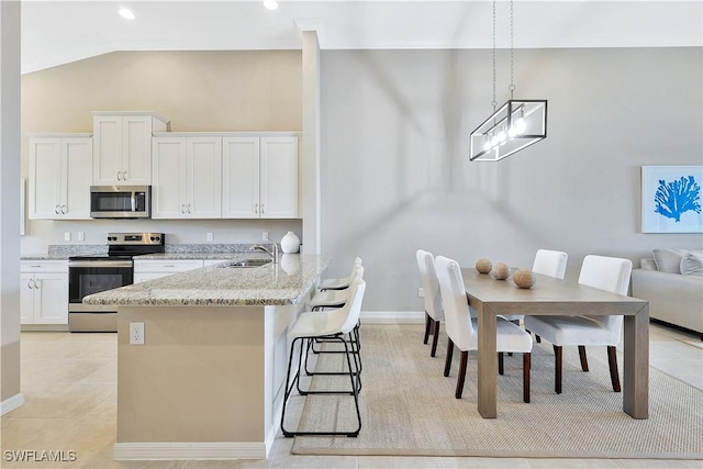 kitchen with a breakfast bar, sink, light stone countertops, white cabinetry, and stainless steel appliances