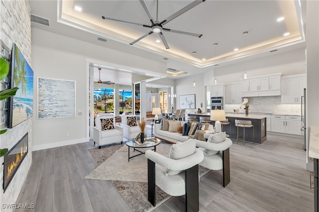 living room with a tray ceiling, ceiling fan, a fireplace, and light wood-type flooring