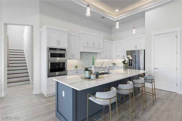 kitchen featuring white cabinetry, an island with sink, decorative light fixtures, a breakfast bar area, and appliances with stainless steel finishes